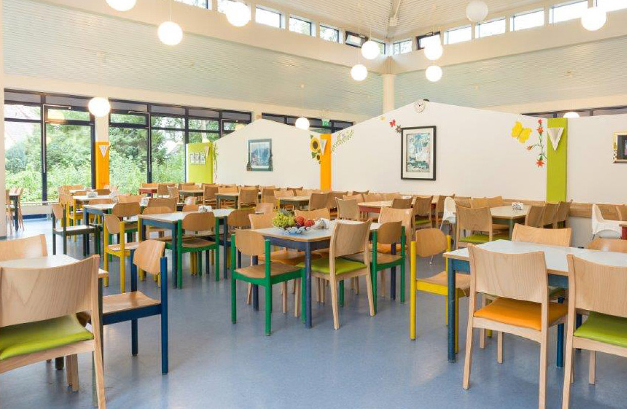 Das geräumige und helle Café der Ostseeklinik Grömitz mit modernen Tischen und Stühlen in verschiedenen Farben. Große Fensterfronten lassen viel Tageslicht herein.