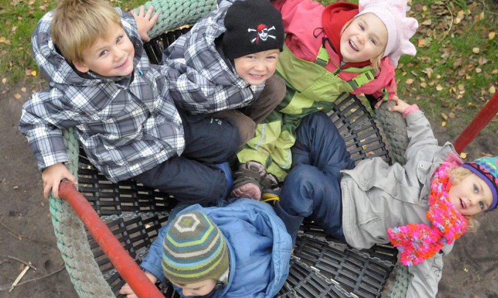Blick von oben, auf spielende Kinder, die gemeinsam in einem Kreis in einer Nestschaukel sitzen, die aussieht wie ein großer geflochtener Korb.