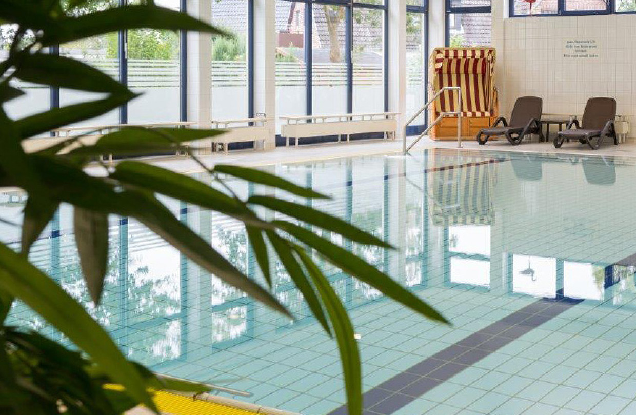 Das helle, innenliegende Therapiebecken des Schwimmbades der Ostseeklinik Grömitz mit blauen Kacheln und einer Rampe für barrierefreien Zugang. Im Hintergrund sind Liegen und ein Strandkorb zu sehen.