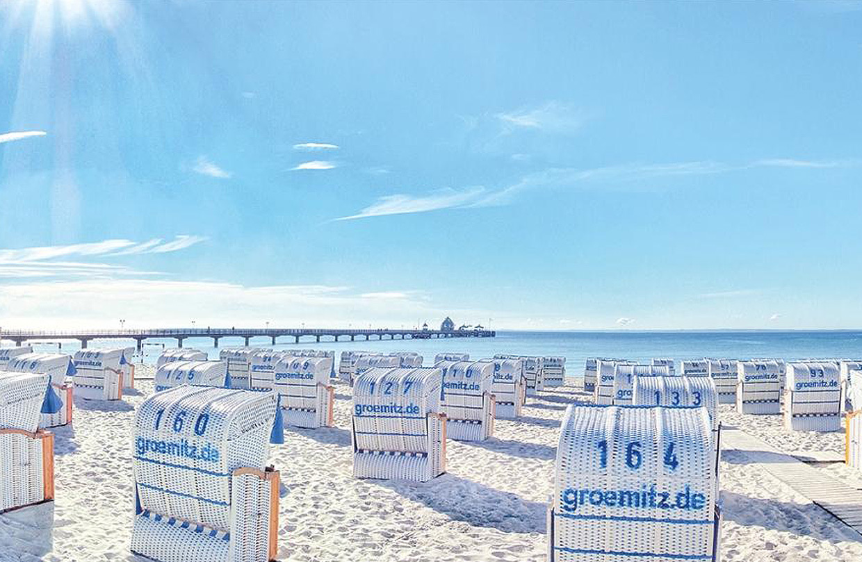 Einladende Küstenlandschaft nahe der Klinik: zahlreiche bunte Strandkörbe am Ostseestrand von Grömitz. Im Hintergrund das blaue Meer unter einem hellen Himmel mit einigen Wolken.