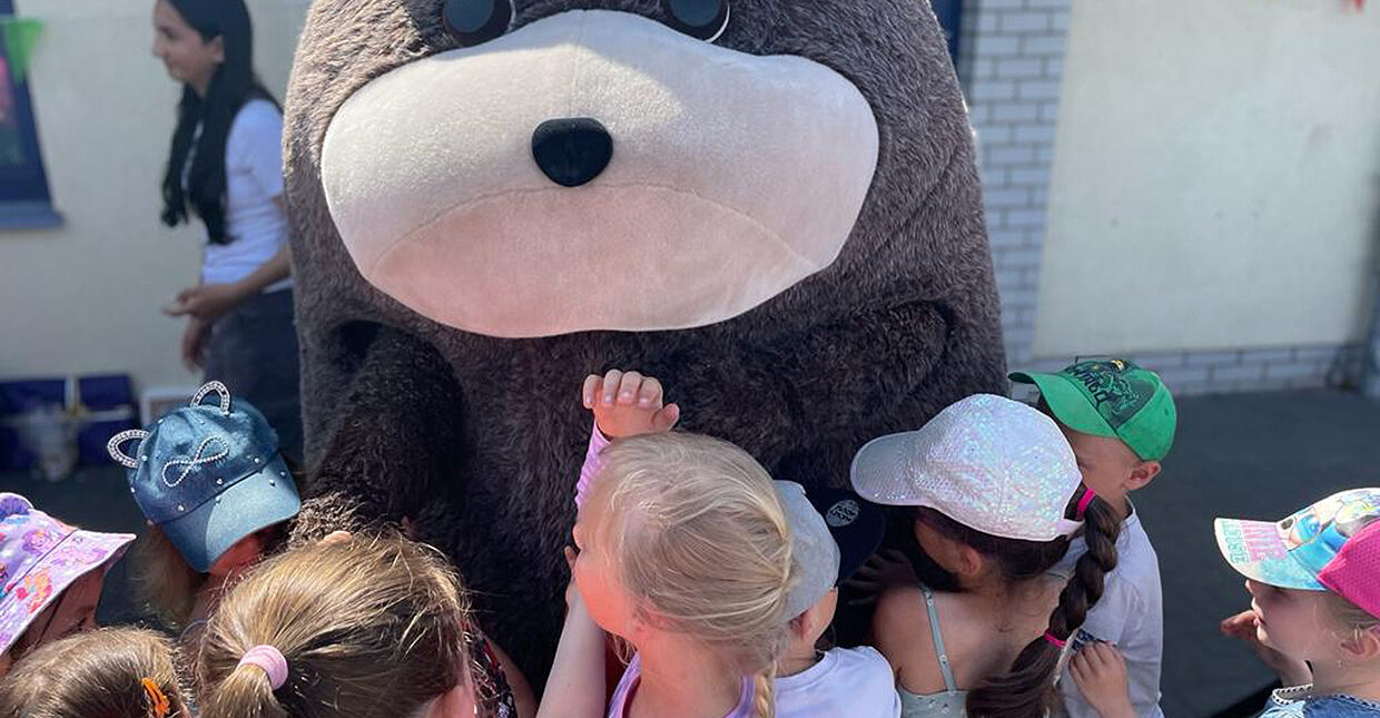 Eine Gruppe von Kindern umarmt Grömel, das große brauche Stofftiermaskottchen.