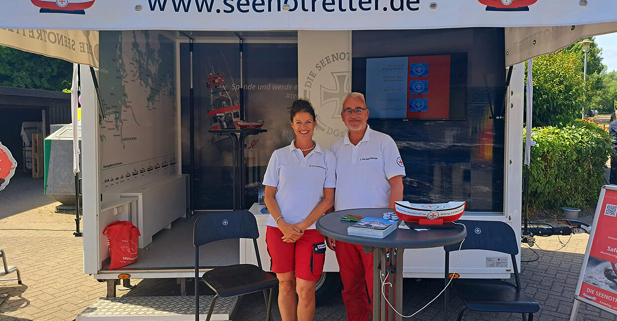 Ein Stand der Seenotretter, vor dem zwei Personen stehen und in Richtung Kamera blicken.